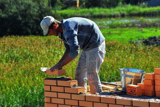 A stonemason building a brick structure on a green pasture.